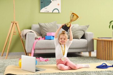 Cute little girl with laptop and rewards for gymnastics at home