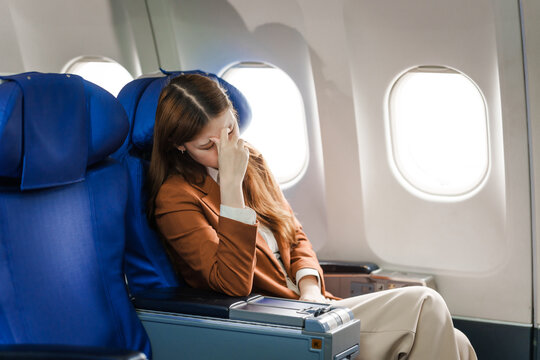 A young Asian woman is sitting in her seat as an airplane passenger, experiencing airsickness with symptoms like nausea, vomiting, dizziness, and general discomfort.