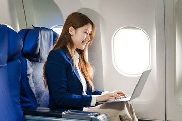 Fototapeta premium A young Asian businesswoman in formal attire sits as an airplane passenger, embodying business travel with technology. She represents professionalism and comfort during her journey.