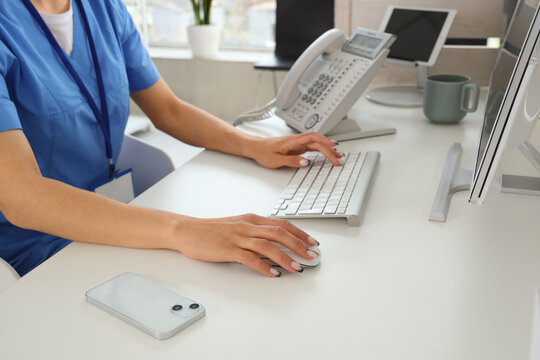Female receptionist working with computer at desk in clinic, closeup