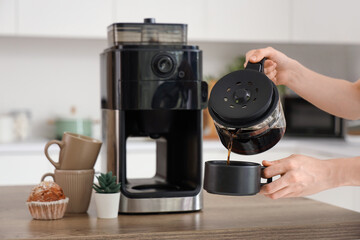 Woman with modern coffee machine pouring espresso from pot into cup in kitchen