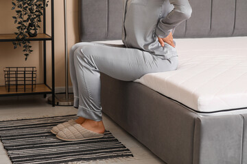 Young woman sitting on soft mattress in bedroom