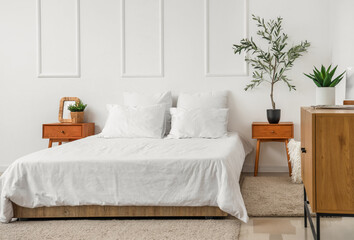 Interior of stylish bedroom with cozy bed, chest of drawers and olive tree on bedside table