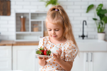Little girl adding cream to plate with strawberries in kitchen
