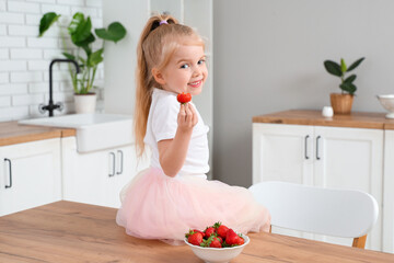 Little girl sitting on table and eating delicious strawberries in kitchen