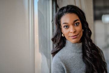 Close-up portrait of a young african-american woman standing at the window and looking at camera