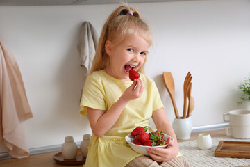 Little girl eating yummy strawberries in kitchen