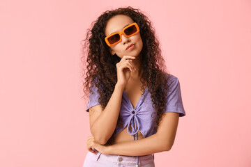 Thoughtful young African-American woman in sunglasses on pink background