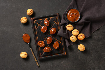 Board with tasty walnut shaped cookies and boiled condensed milk on black grunge table