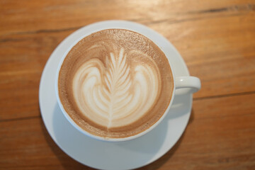 Hot latte art coffee in white ceramic cup on wooden table.