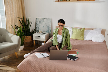 A woman sitting on a bed, focused on her laptop screen.