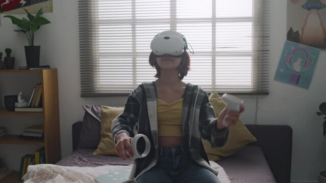 Full shot of teenage girl in process of playing game using vr headset and swinging controllers in bedroom