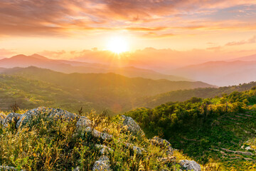 Obraz premium highland mountain landscape of beautiful sunset or sunrise with nice mountain peaks and slopes, green and golden hills and majestic cloudy sky on background