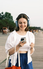 Smiling young woman listening music with wireless headphones outdoor in the park