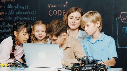 Closeup of boy using laptop programing engineering code and writing program while group of diverse...