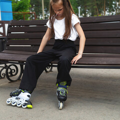 Child girl puts on roller skates in park closeup