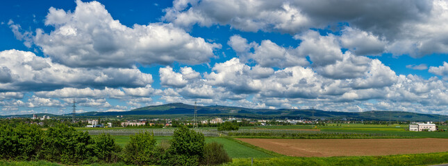 Panoramafoto über das Rhein-Main-Gebiet mit dem Mittelgebirge Taunus am Horizont und aufgelockertem Himmel mit Haufenwolken bei sonnigem Wetter