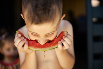 Cute kids in swimsuits sitting on a porch and eating fresh ripe watermelon.