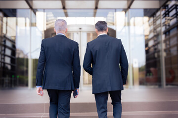 Fototapeta premium two caucasian male business colleagues talking happily, co-workers talking walking to enter the office building where they work