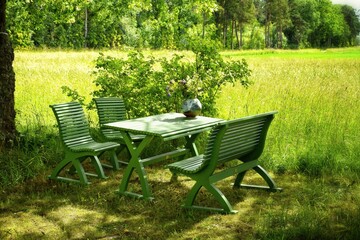 Green wooden table, bench and chairs. A place to relax in nature.