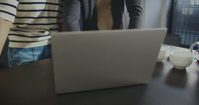 Wonderful Asian couple spending time together in middle of their large modern kitchen. Opening lid of laptop and beginning conversation online. Waving their hands to relatives or friends.