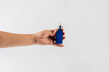 Blue glass cosmetic bottle in hand, Skin care or sunscreen cosmetic on white background.