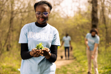 African american young activist holding a small vegetation sprout with organic soil, working on...