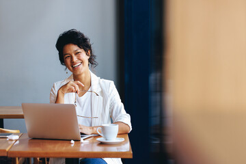 Smiling businesswoman working at a cafe with laptop and coffee