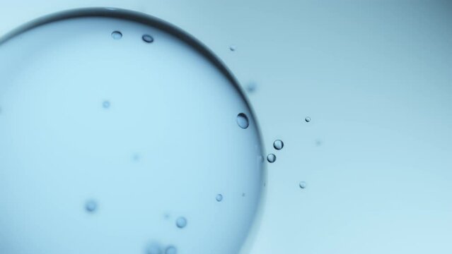 Macro shot of drops of pure fresh melt mountain water with tiny air bubbles, small droplets separate from the large water sphere and fly away on a bright light blue background