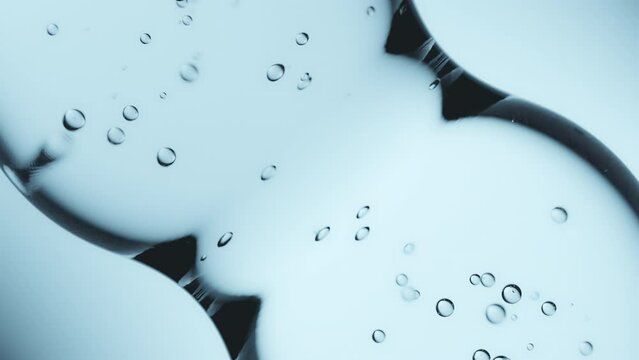 Macro shot of drops of pure fresh melt mountain water with tiny air bubbles, the drops are moving and merging into a large water sphere on a bright light blue background