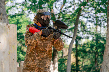 in the wild near tree structures player in a pintball uniform holds a pistol with a red balloon...