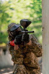 Fototapeta premium close up in the wild near tree structures player in a pintball uniform holds a pistol with a red balloon team game camouflage clothing