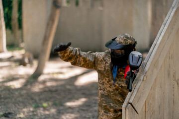 in the wild near tree structures player in a pintball uniform holds a pistol with a balloon team game camouflage clothing communication using hands