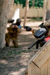 in the wild near tree structures player in a pintball uniform holds a pistol with a balloon team game camouflage clothing communication using hands