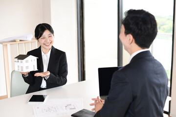 住宅模型を使い提案するスーツ姿の若い女性
