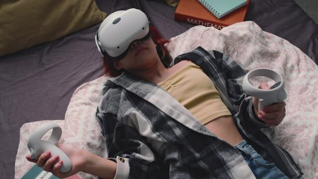 Top view of gen alpha girl lying in bed with vr goggles and controllers, choosing movie or playing