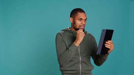 Angry man fighting with friend during videocall on tablet, isolated over studio background. Rude...