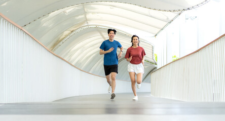 Young Asian couple exercising jogging outdoors in park. Happy runner in sports clothing running...