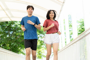 Young Asian couple exercising jogging outdoors in park. Happy runner in sports clothing running outside in urban city in the morning. Wellbeing healthy lifestyle person. Copy space.