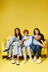 Fototapeta premium Young multicultural friends in stylish attire sitting on top of a yellow couch, enjoying each others company.