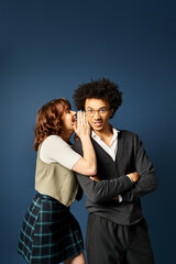 A young multicultural man, a woman, stand together in stylish attire against a dark blue background.