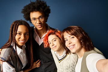 Fototapeta premium Young multicultural friends, including a nonbinary person, stand together in stylish attire, posing for a picture on a dark blue background.