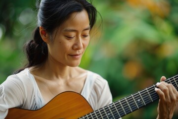 Portrait of a blissful asian woman in her 30s playing the guitar in soft green background