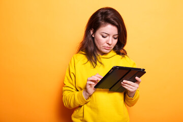 Focused female entrepreneur browsing the internet on her tablet, researching on business market. Portrait of woman wearing a hoodie and using digital device for online communication.