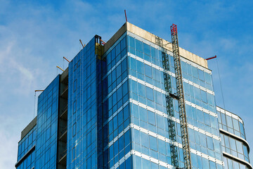 Fototapeta premium Precast glass facade panels installation, building under construction against sky background. Glass panel installation, cladding wall. Symmetry and industrial design elements of the glass structure