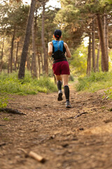 A woman runs through a forest trail wearing a blue and red outfit. She is wearing black socks and a black hat