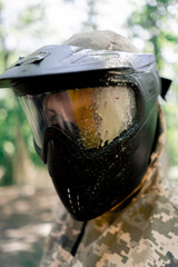 Fototapeta premium close up in the forest pintball player in uniform in a black protective mask on his face a yellow stain from a paint ball team competition