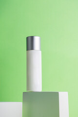 Plastic white tube for cream or lotion. Skin care or sunscreen cosmetic with stylish props on green background.