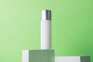 Plastic white tube for cream or lotion. Skin care or sunscreen cosmetic with stylish props on green background.