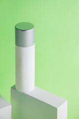 Plastic white tube for cream or lotion. Skin care or sunscreen cosmetic with stylish props on green background.